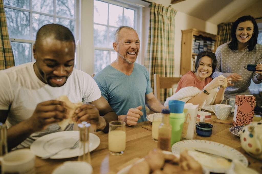 Holiday guests and family eating breakfast and laughing together at a kitchen table